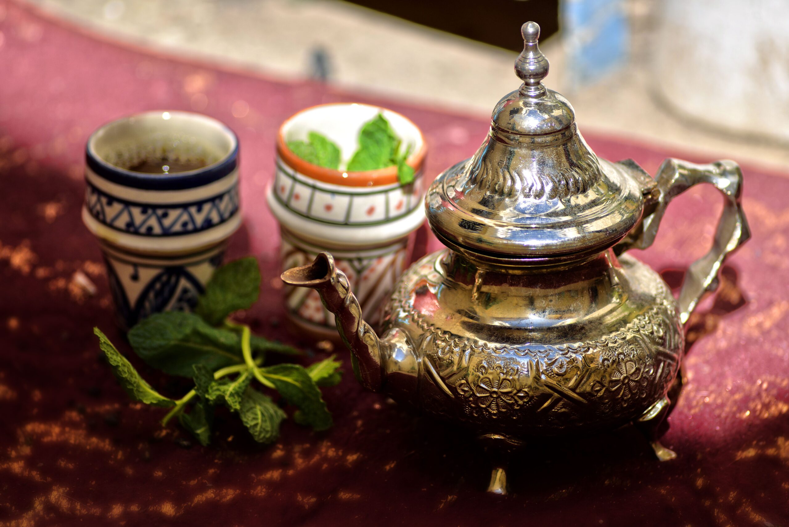 An authentic Moroccan Mint Tea setup with a traditional engraved metal teapot and fresh mint leaves